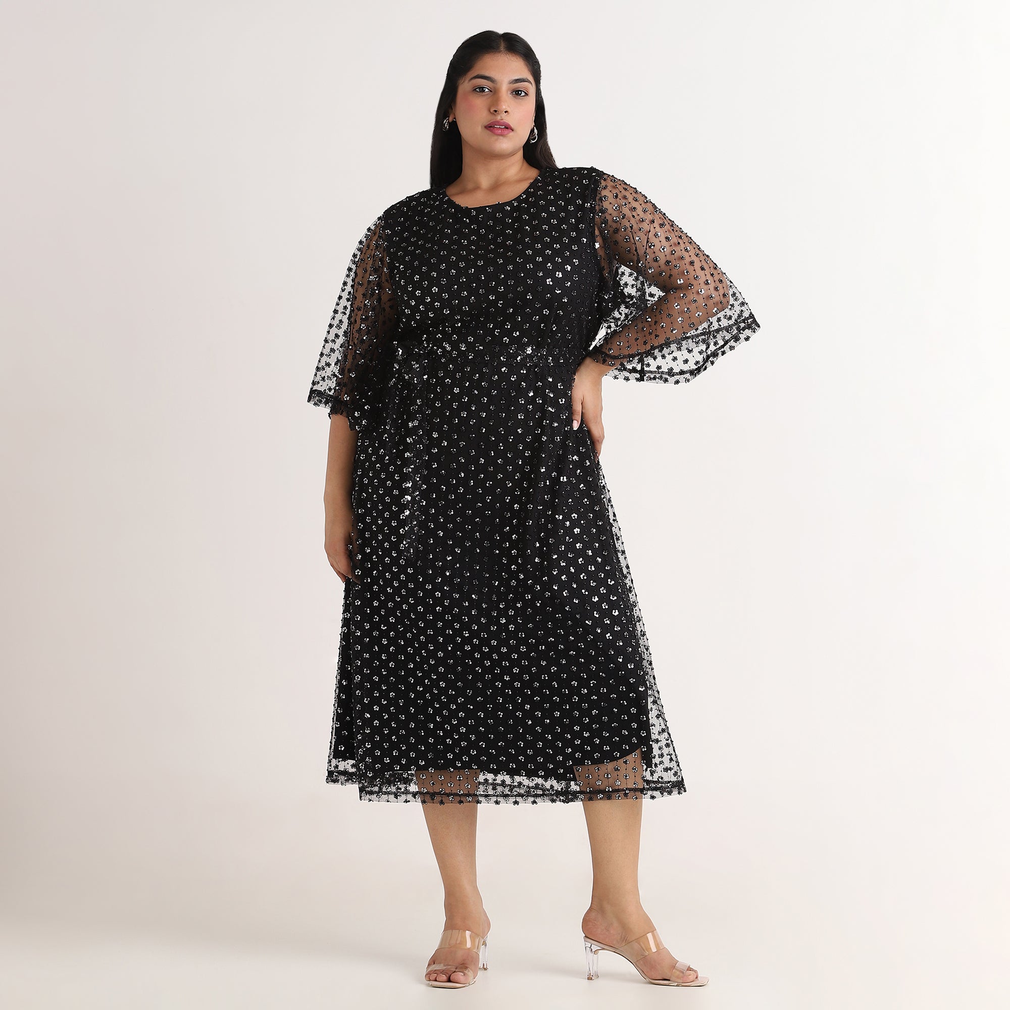 Woman wearing a black dress with sheer sleeves on a white background