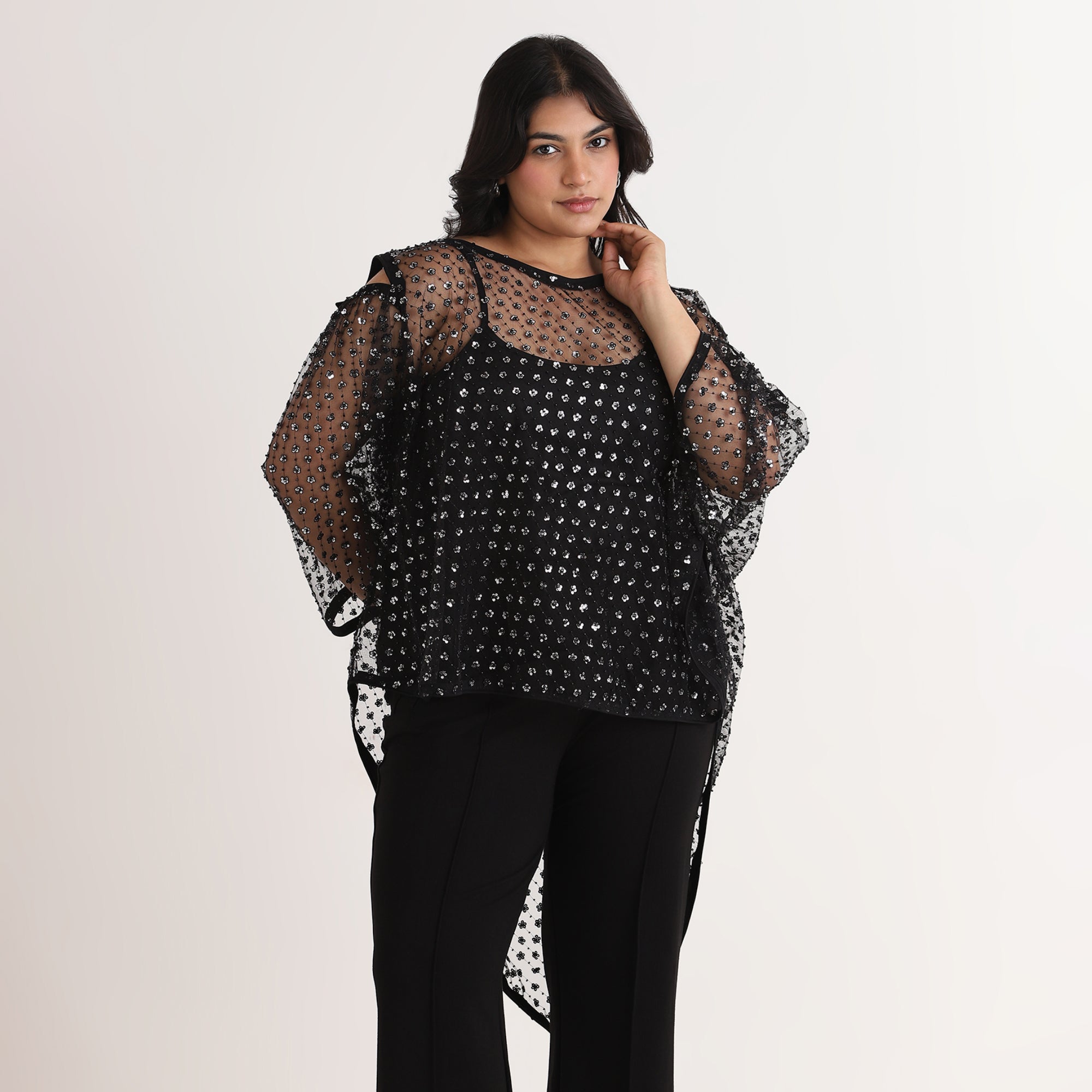 Woman wearing a black sheer kaftan top with polka dot pattern on a white background