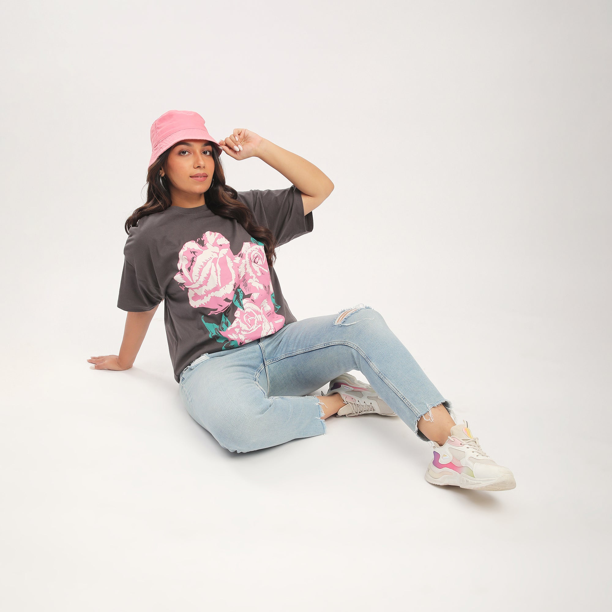 Person sitting on the ground wearing a graphic t-shirt, jeans, and sneakers.