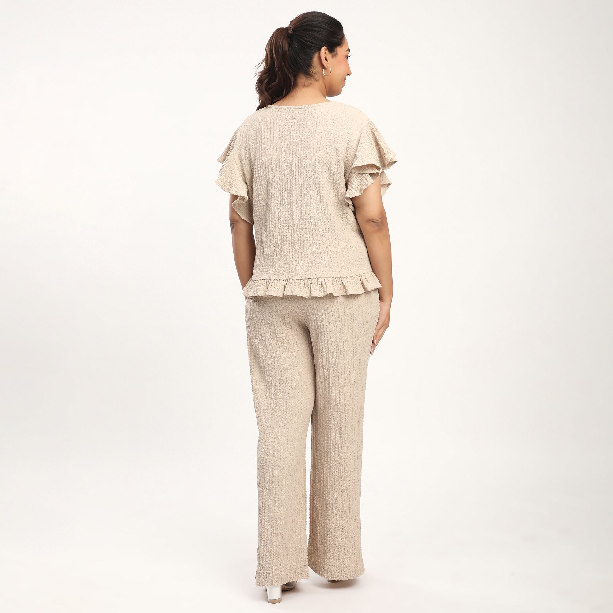 Person wearing a beige outfit with ruffled sleeves on a white background