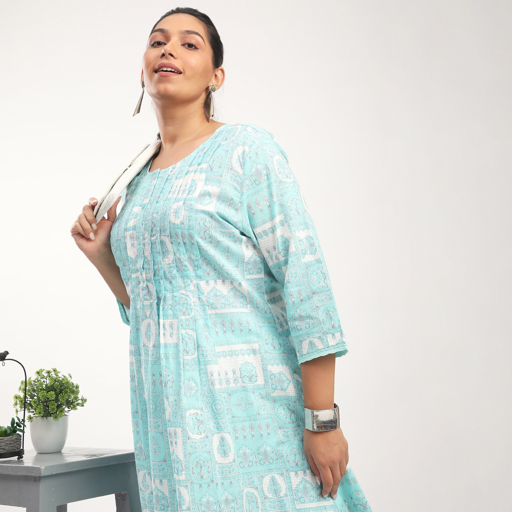 Woman in a light blue patterned dress holding a bag against a white background