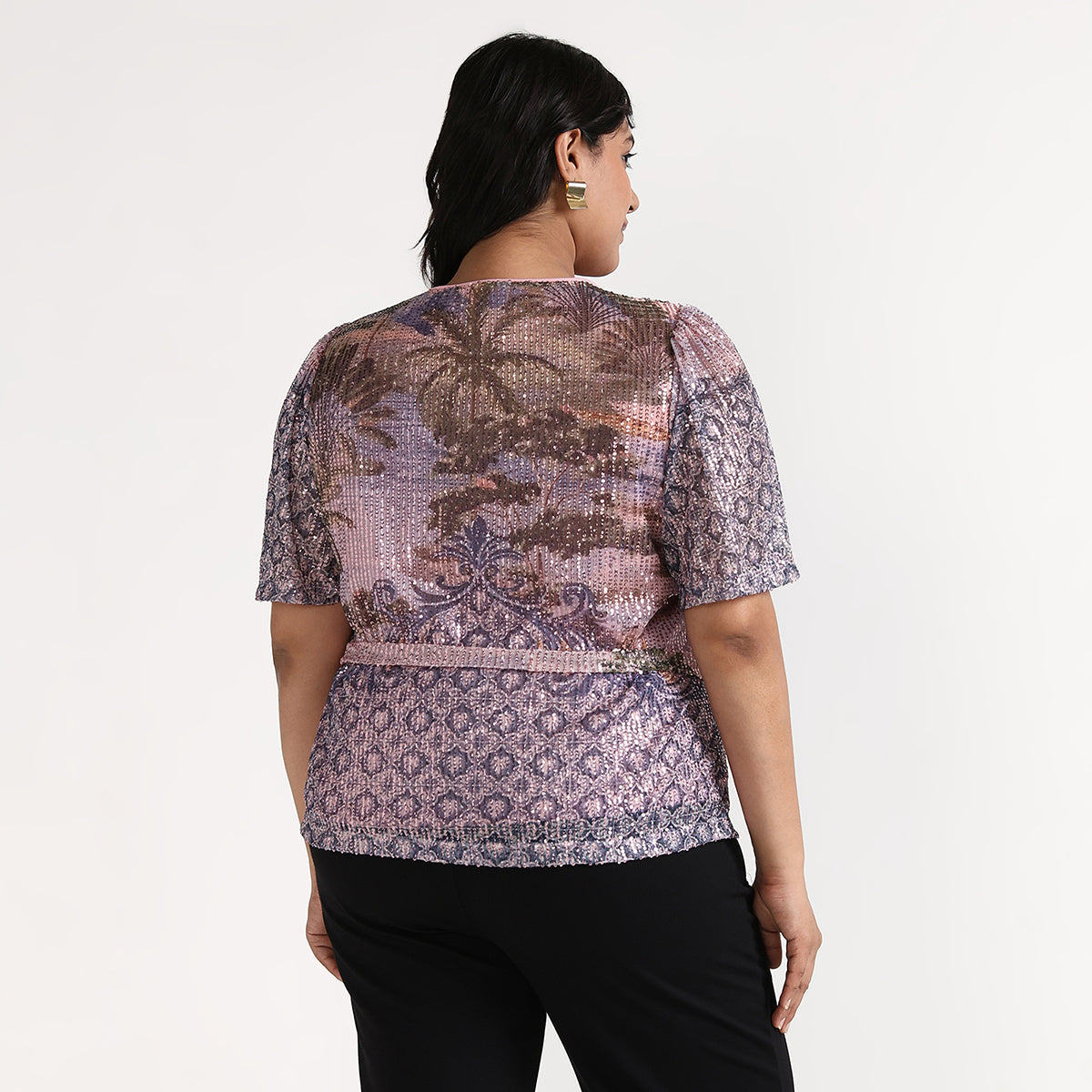 Woman wearing a patterned top and black pants on a white background