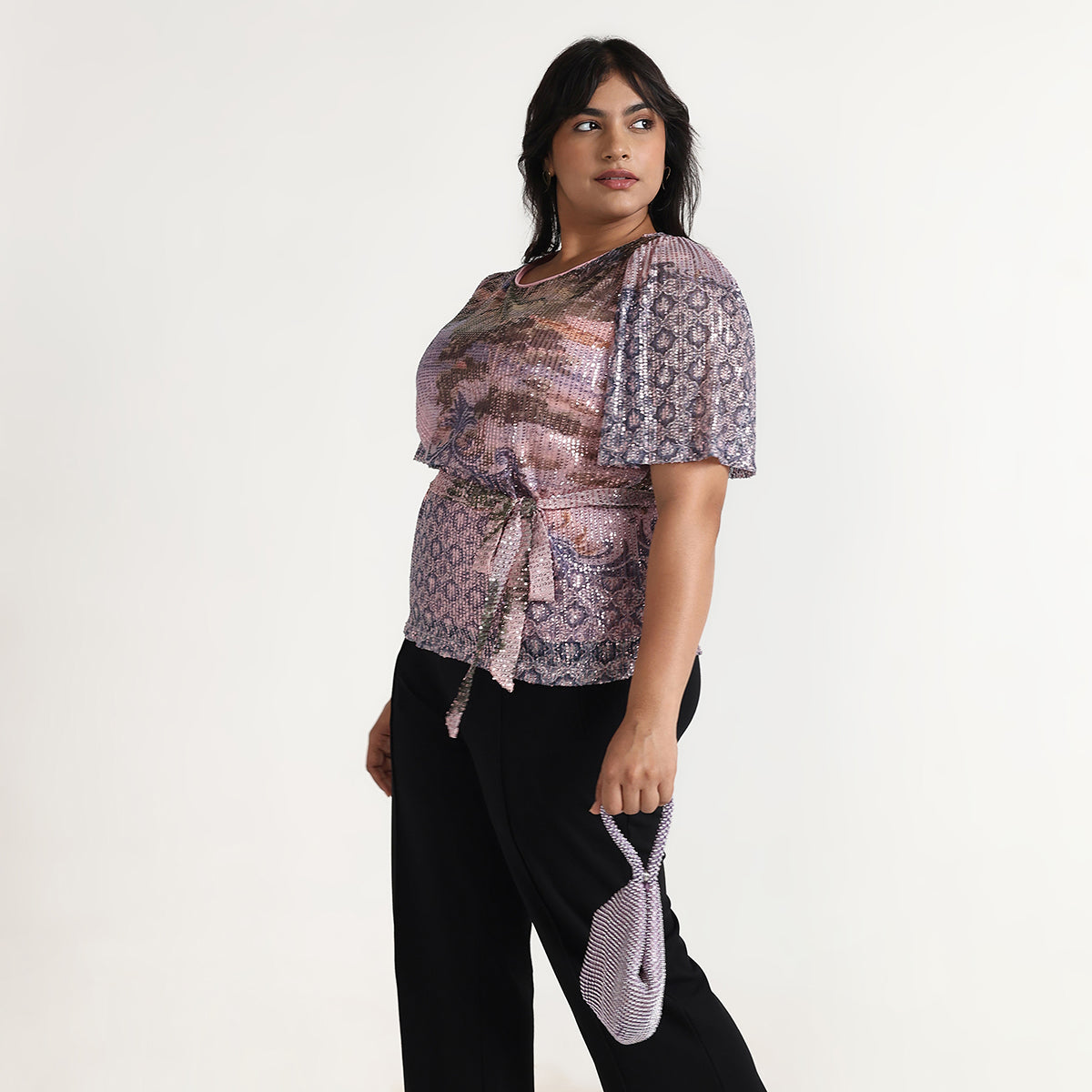 Woman wearing a patterned top and black pants against a white background