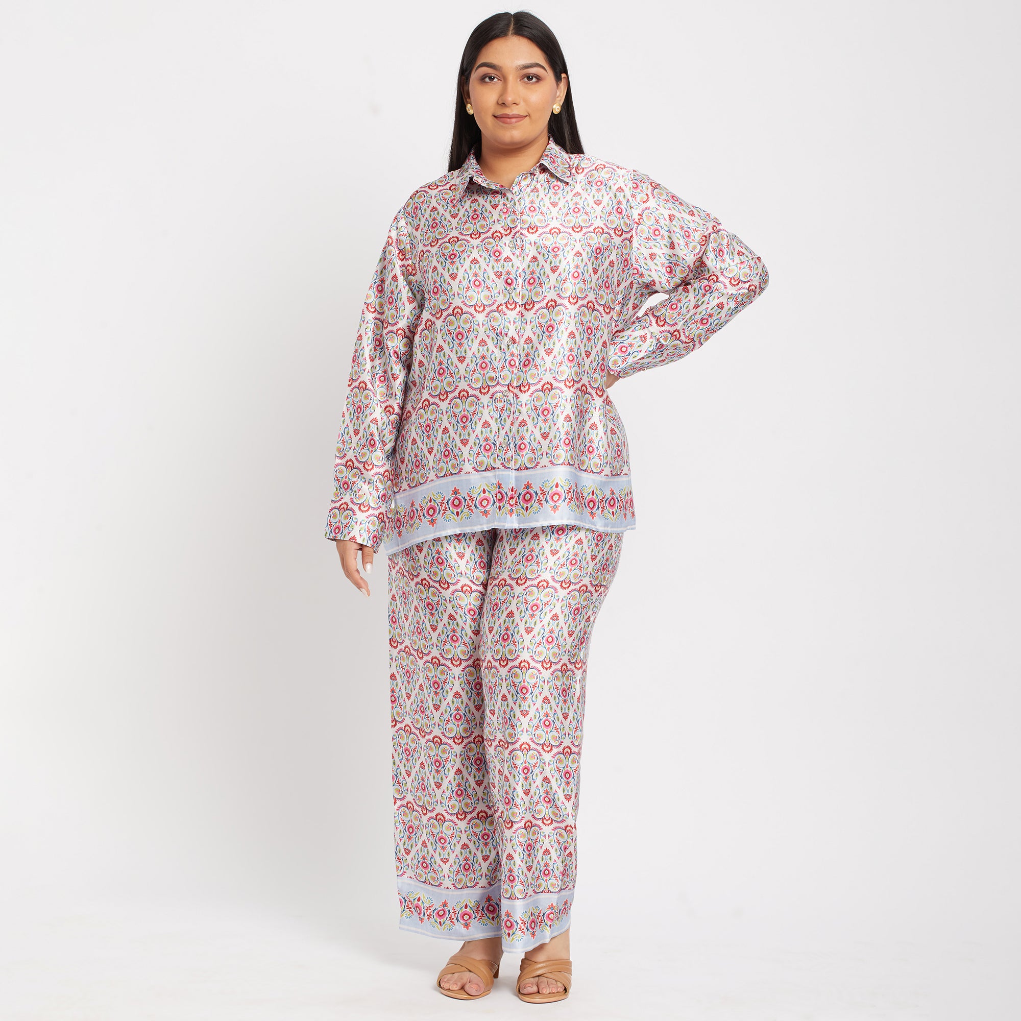 A woman wearing a white and red floral satin plus size co-ord set with long sleeves and relaxed fit bottoms.