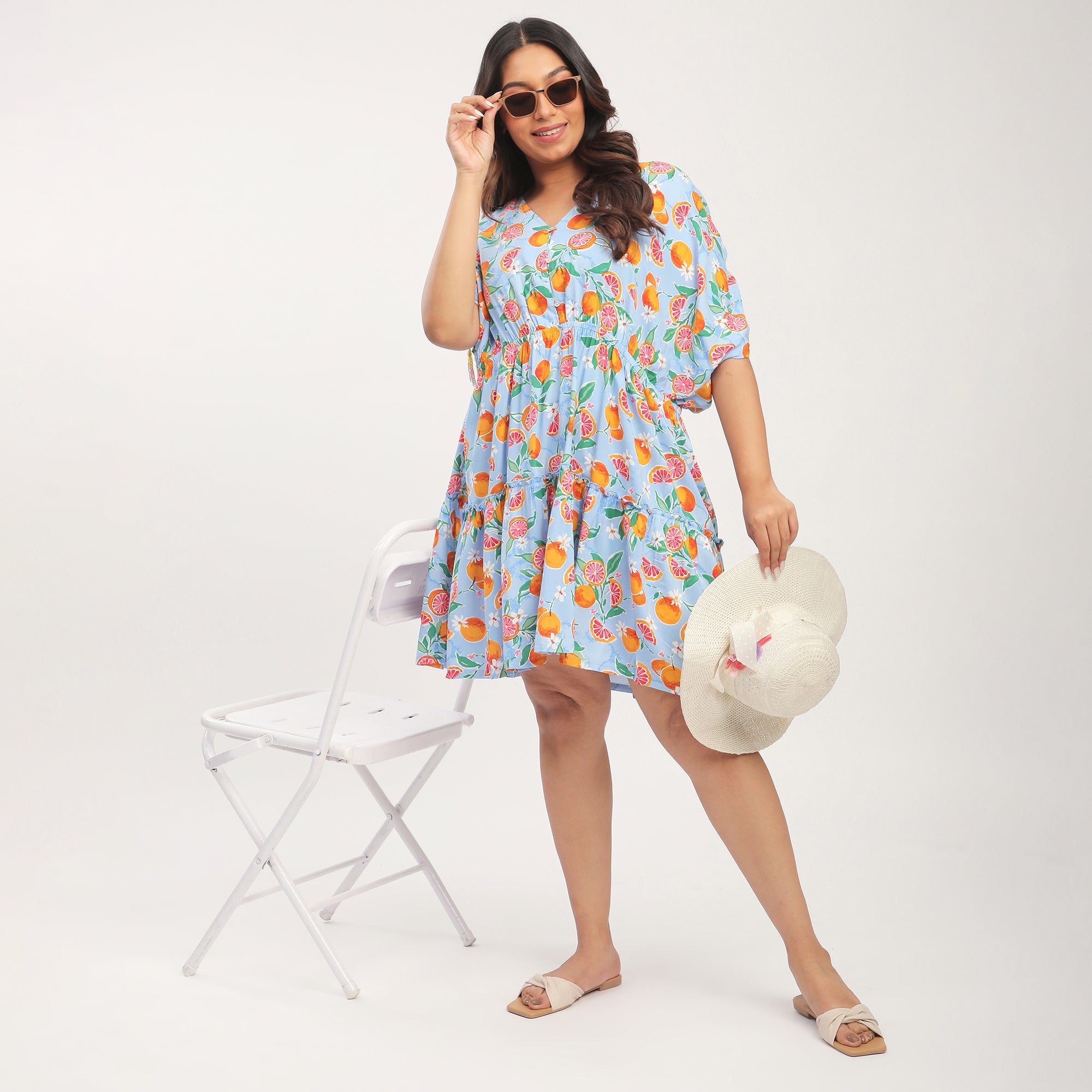 Woman in a colorful floral dress holding a hat against a white background