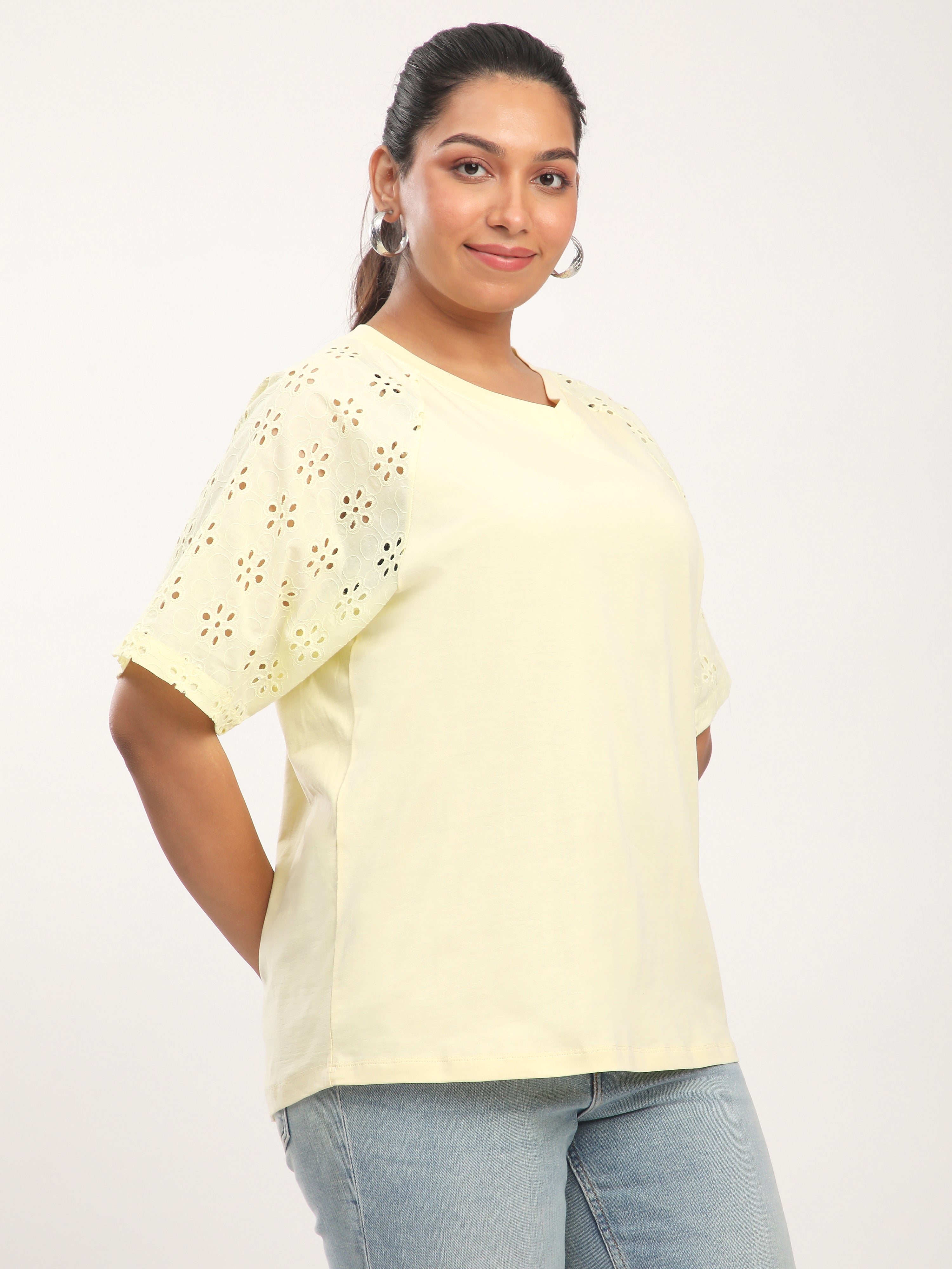 Woman wearing a light yellow top with lace details on a white background