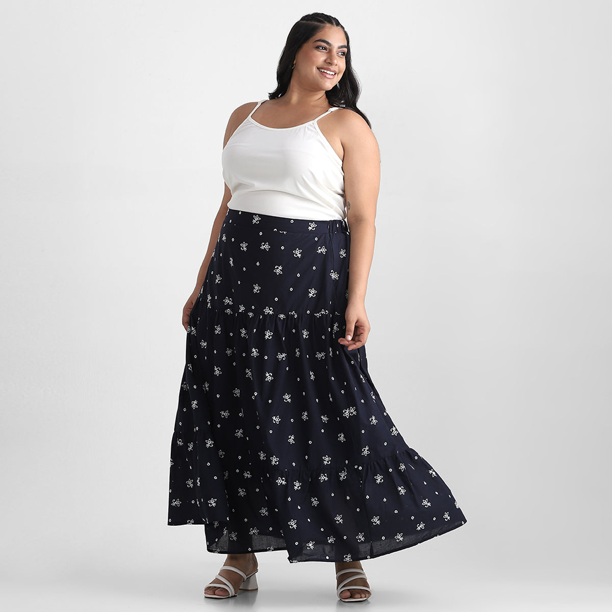 A plus-size model wearing a navy maxi skirt with a floral pattern and a white tank top.