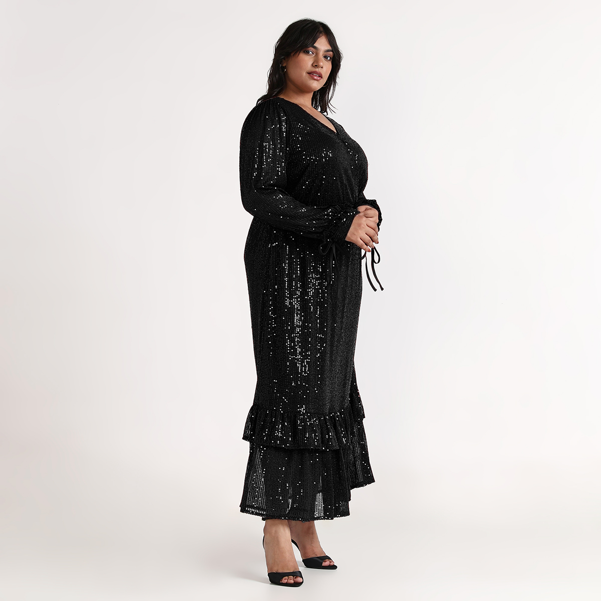 Side view of women wearing black sequin maxi dress with flowy tiered design